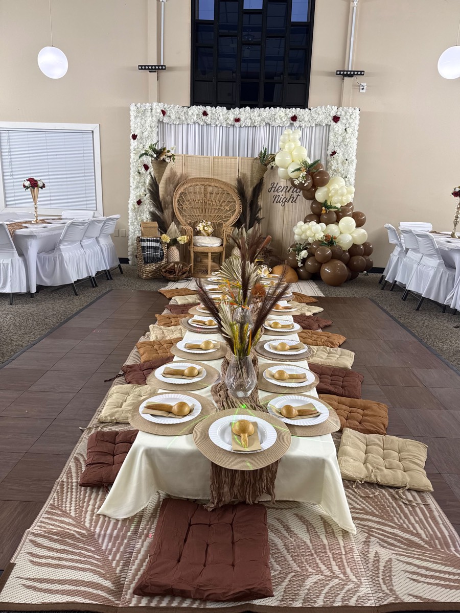 A Henna Night table with woven placemats and cushions leading to a rattan chair and balloon garland